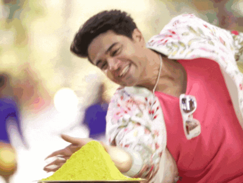 a man in a pink shirt is holding a pile of yellow powder in his hand