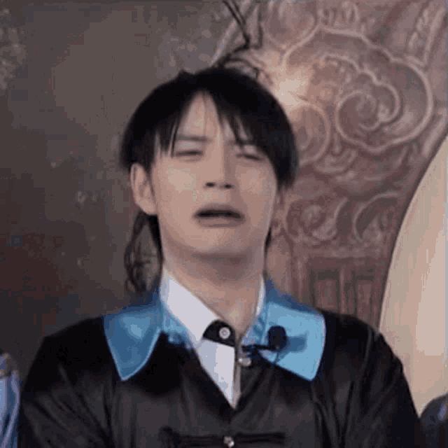 a man in a black jacket and blue tie is making a funny face with his mouth open .