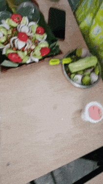 a bowl of vegetables sits on a wooden table next to a cell phone