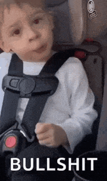 a young boy is sitting in a car seat with a seat belt on and making a funny face .