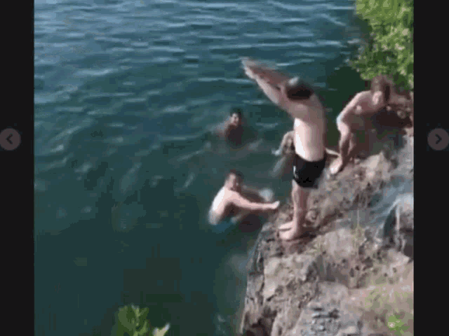 a group of people are jumping into a body of water from a cliff .