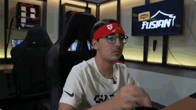 a man wearing glasses and a red headband is sitting in front of a tv that says fusion