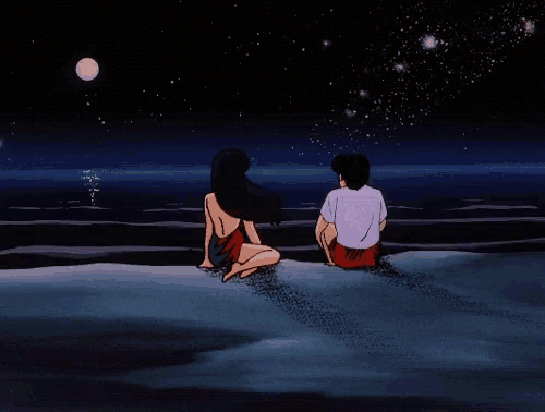 a man and a woman are sitting on a beach looking at the moon