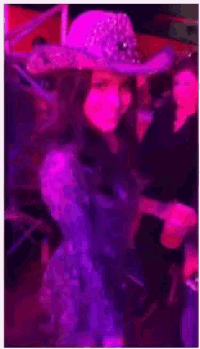 a woman wearing a cowboy hat is dancing in a pink and purple light .