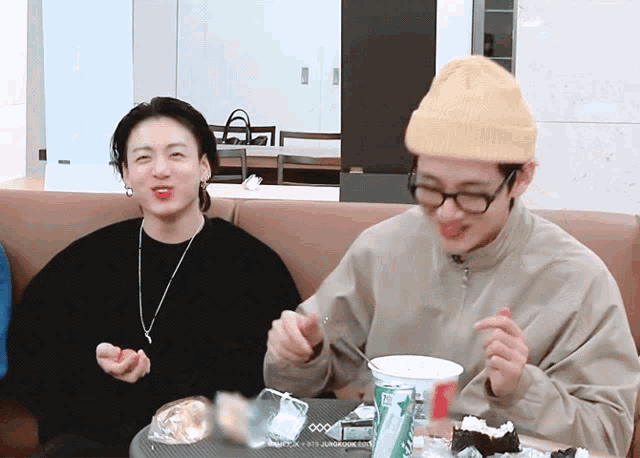 two young men are sitting on a couch eating food and one of them is wearing a beanie
