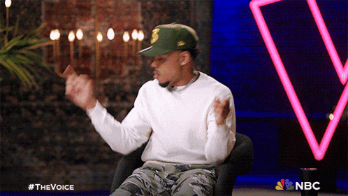 a man wearing a green hat is sitting in a chair in front of a nbc logo