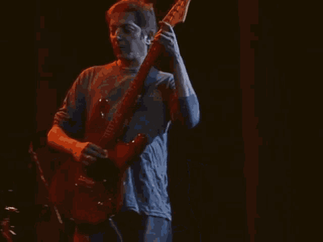 a man in a blue shirt is playing a guitar on a stage