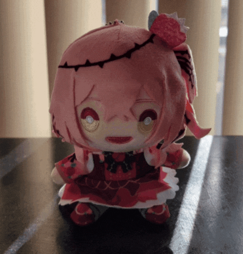 a stuffed doll with pink hair and a red dress is on a table