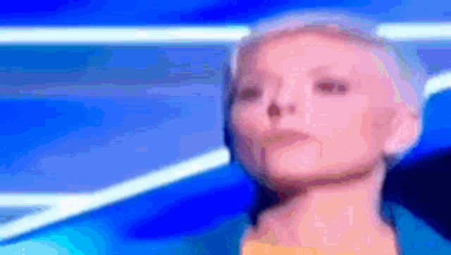 a woman with short hair is standing in front of a blue background and looking at the camera .