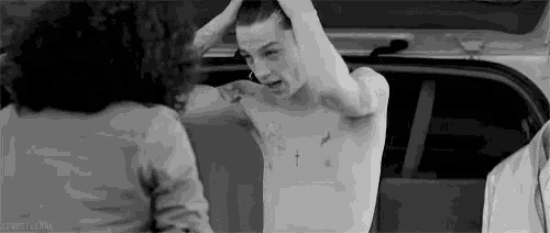 a man without a shirt is standing in the back of a car with his hands in his hair .
