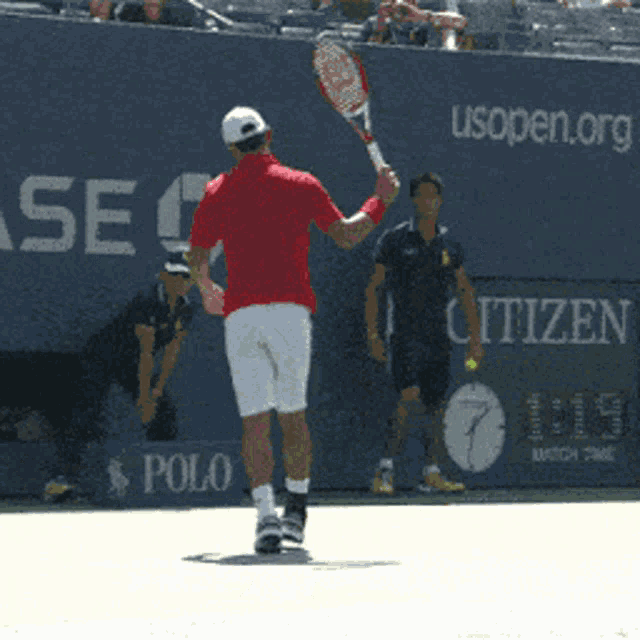 a man in a red shirt is holding a tennis racquet in front of a wall that says polo