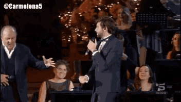 a man in a tuxedo sings into a microphone while standing next to another man