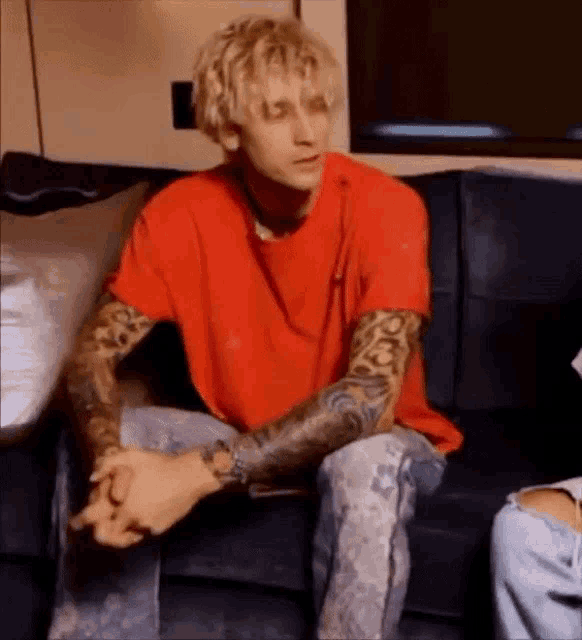 a man in a red shirt is sitting on a couch with his arms crossed .