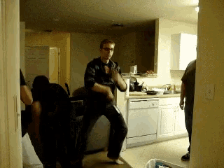 a man is dancing in a kitchen with other people watching