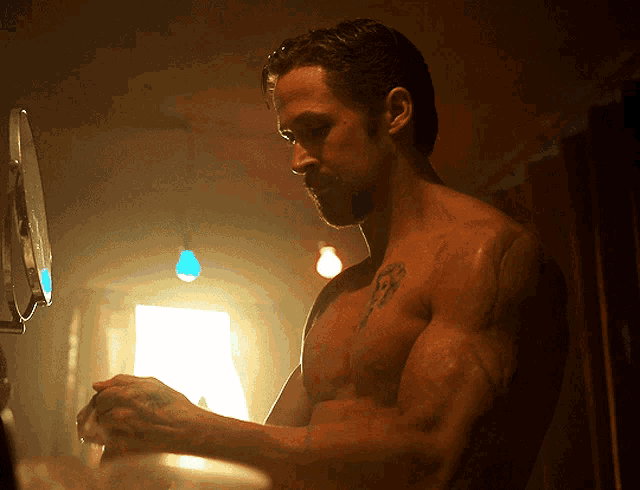 a shirtless man with a tattoo on his chest is looking at himself in a mirror