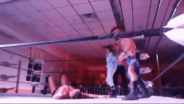 a wrestler is laying on the ground in a wrestling ring while a referee stands behind him .
