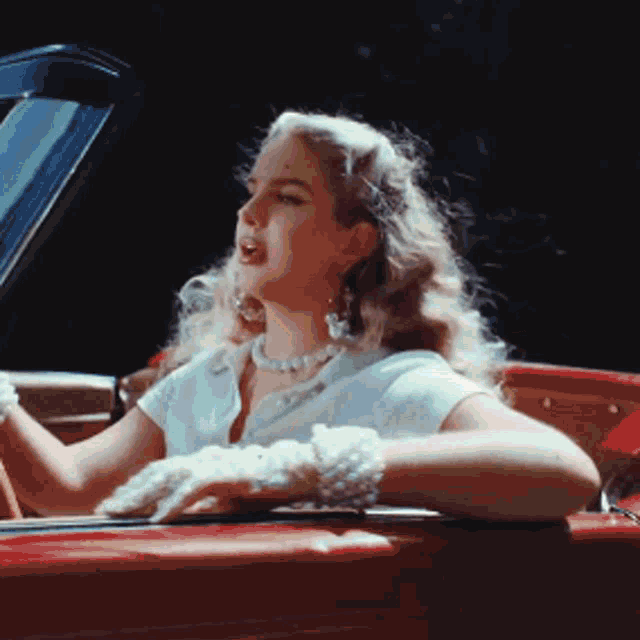 a woman in a white shirt and white gloves is sitting in a red convertible car .