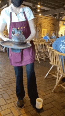 a waitress wearing a purple apron is carrying a tray with a pitcher on it