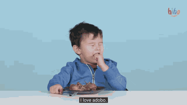 a little boy is sitting at a table with a plate of food and says i love adobo .