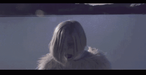 a woman in a white fur coat is standing in front of a lake .
