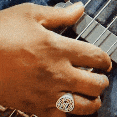 a close up of a person playing a guitar with a ring on their finger that has the letter g on it