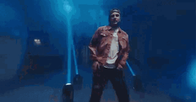 a man in a pink jacket and sunglasses is dancing on a stage in a dark room .