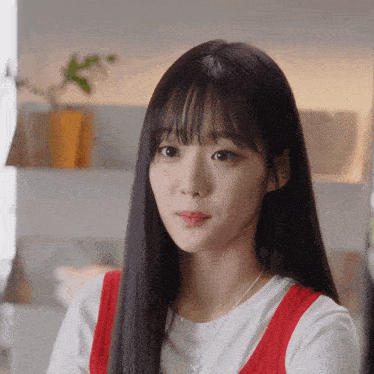 a woman with long black hair and bangs wearing a white shirt and a red vest