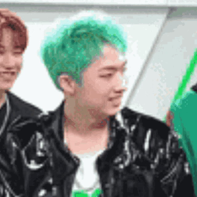 a man with green hair is wearing a black jacket and a green shirt .
