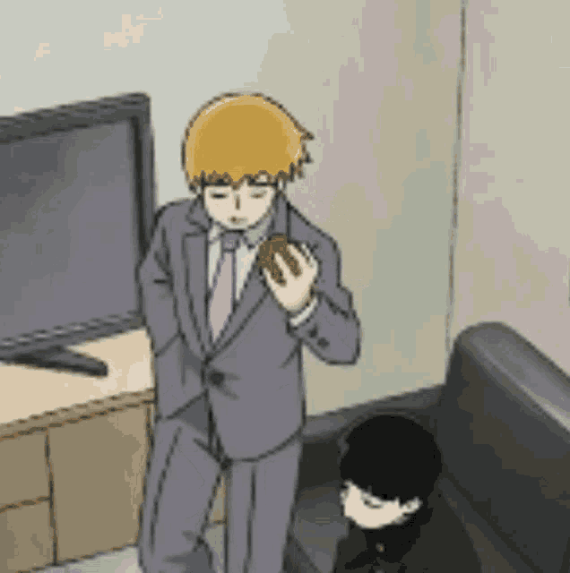 a man in a suit and tie is standing next to a couch and a television .