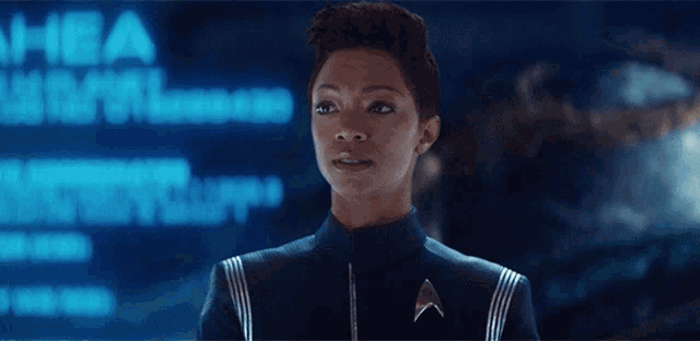 a woman in a star trek uniform stands in front of a screen that says " hba "