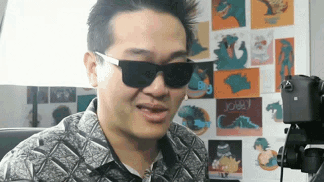 a man wearing sunglasses stands in front of a wall that has a picture of a dinosaur and the word joey