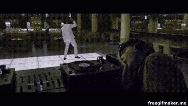 a man in a white suit is dancing on a dance floor in front of a dj .