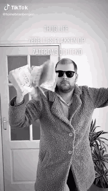 a man wearing sunglasses and a coat is holding a roll of toilet paper