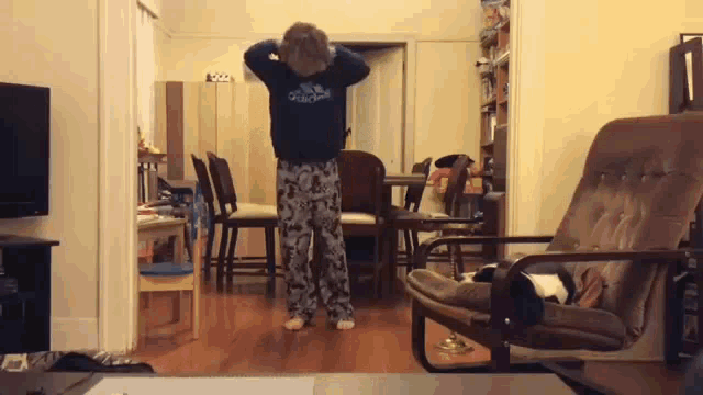 a young boy is dancing in a living room with a chair .