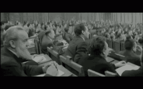 a black and white photo of a large group of people sitting in a classroom .