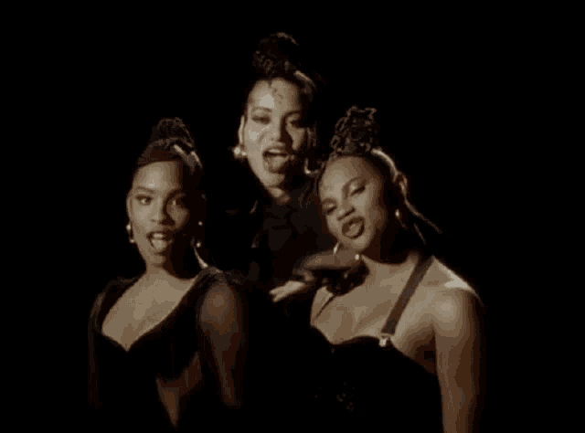 a group of three women are standing next to each other in a dark room