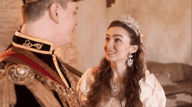 a woman wearing a tiara and earrings looks at a man in a costume