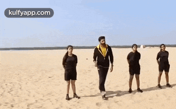 a man is standing on a sandy beach with two women standing behind him .