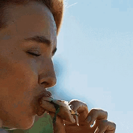 a close up of a person eating a sandwich with their eyes closed