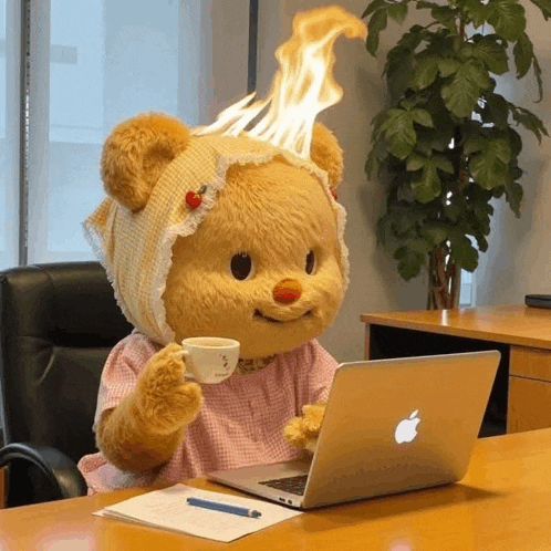 a teddy bear sitting at a desk with an apple laptop and a cup of coffee