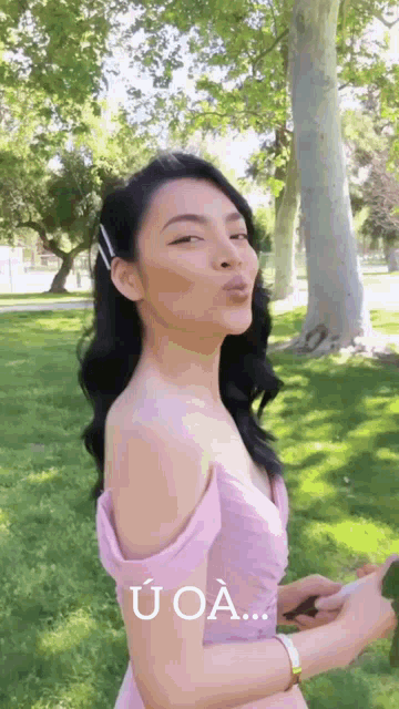 a woman in a pink dress is blowing a kiss in the park .