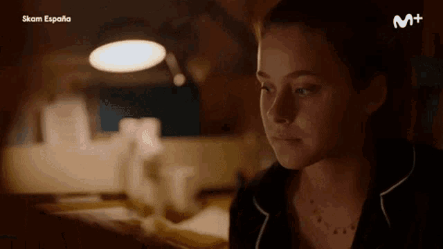 a woman is sitting at a table with a lamp and the word m+ on the bottom