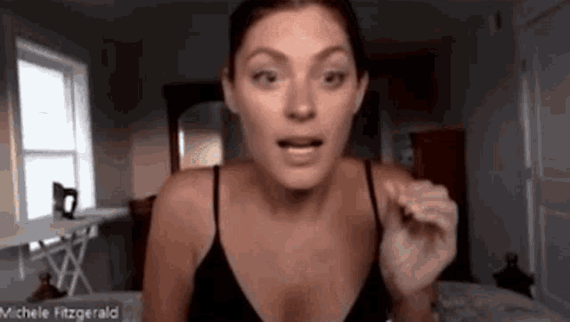 a woman in a black tank top is making a funny face while sitting in front of a window .