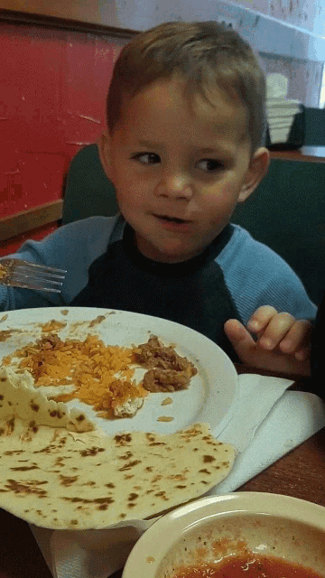 a young boy is sitting at a table with a plate of food in front of him