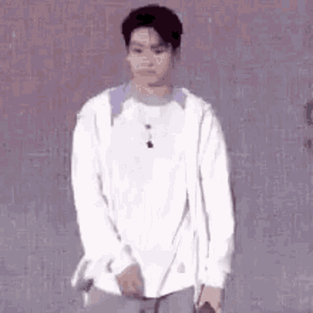 a young man wearing a white shirt and a white jacket is standing in front of a wall .