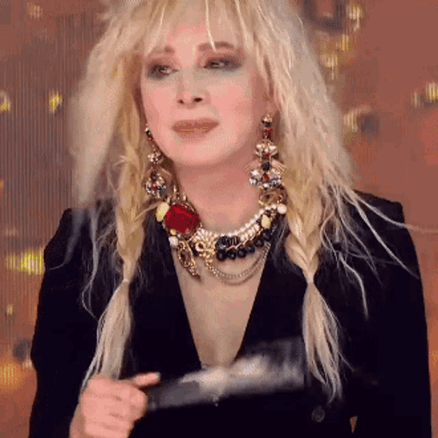 a woman with blonde hair wearing a black jacket and necklace