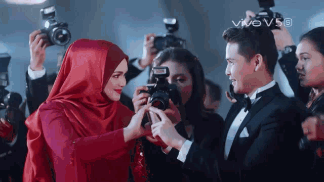a man in a tuxedo is taking a picture of a woman in a red dress
