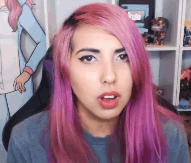 a woman with pink hair and a gray shirt is making a face
