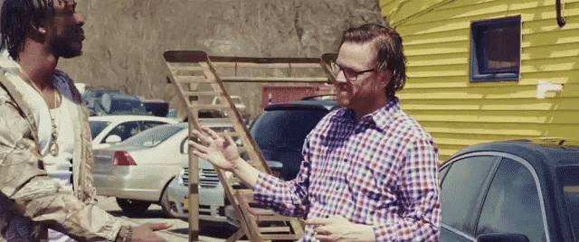a man in a plaid shirt is talking to another man in front of a yellow building