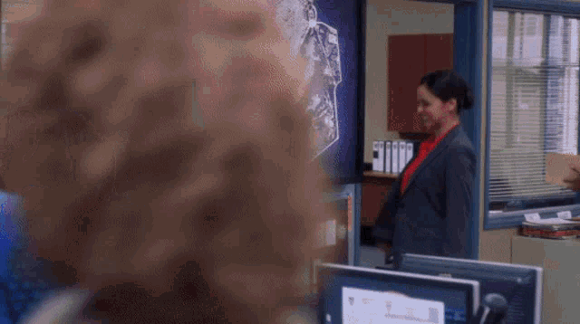 a woman in a suit and red shirt is standing in front of a computer monitor